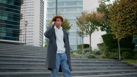 relaxed teenager walking stairs at city street. young man calling earphones