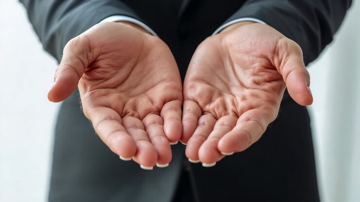 Professionele handen en onderarmen uitgestrekt, handpalmen in een kom naar de lens in een kantoor, witte manchetten zichtbaar