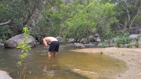 shirtless adult male standing in swimming hole washing face in emerald creek