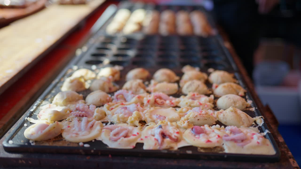 Close up of squid dumplings being cooked on a cast iron takoyaki grill pan at a street food market in Japan