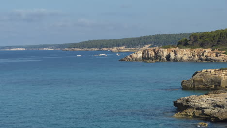 rocky coastline on the island of minorca, several boats at anchor or mooring