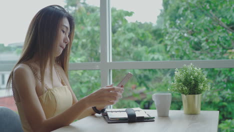 Mobile-payment-concept-:-Young-beautiful-Asian-woman-enjoying-a-relaxing-moment-working-and-using-mobile-phone-as-mobile-smart-payment-to-pay-for-a-coffee-in-the-coffeeshop-on-a-bright-sunny-day