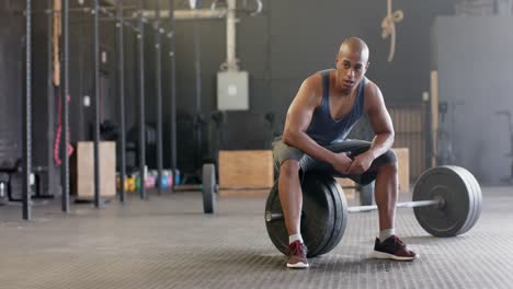 Tired-biracial-man-sitting-on-barbell-resting-after-weight-lifting-at-gym,-slow-motion,-copy-space