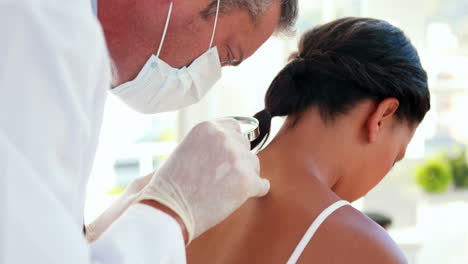 el médico examinando la espalda de su paciente con una lupa