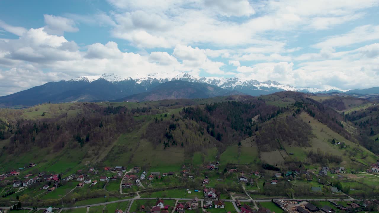 Gazing at the Enchanting Beauty of Bucegi Mountains- A Captivating Drone Perspective of Snowy Summits, Charming Mountain Village, and Serene Green Fields in Romania's Transylvania