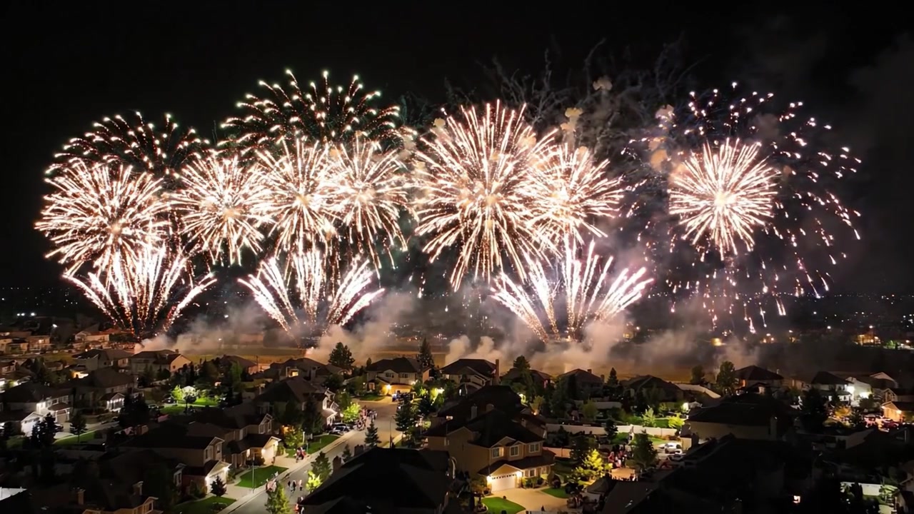 En spektakulær nattehimmel oplyst af farverigt fyrværkeri over forstadshuse, der skaber et fantastisk visuelt skue af lys og lyd i mørket.