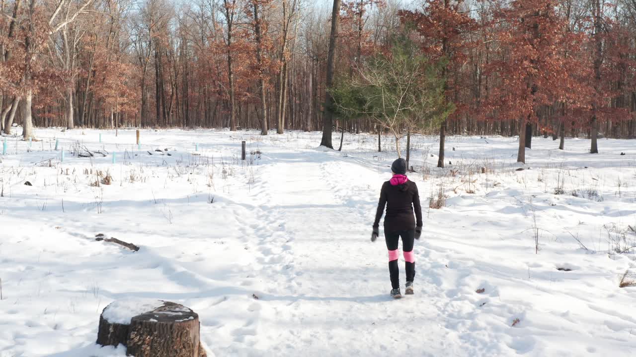 Mulher com roupa de exercício quente caminhando sozinha em um caminho florestal coberto de neve