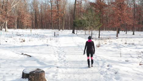 mujer con ropa de ejercicio caliente caminando sola en un camino forestal cubierto de nieve