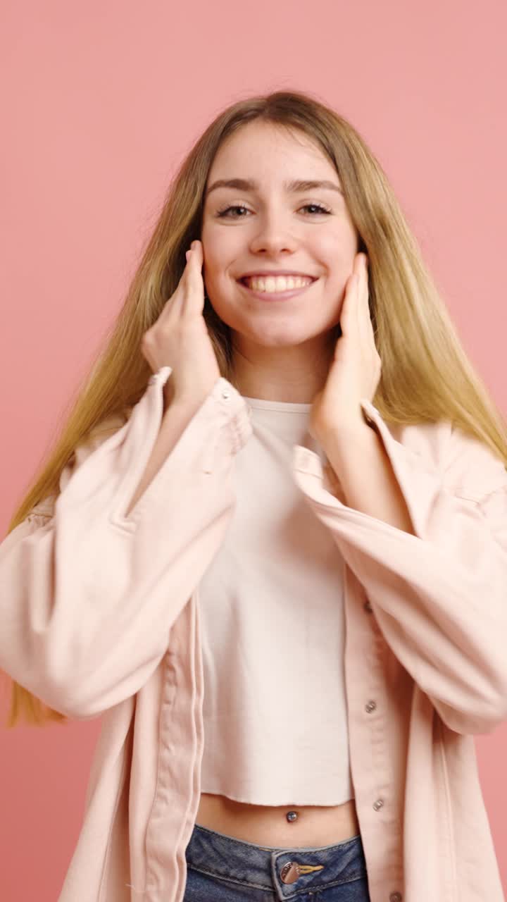 Young woman expressing surprise and happiness on pink background