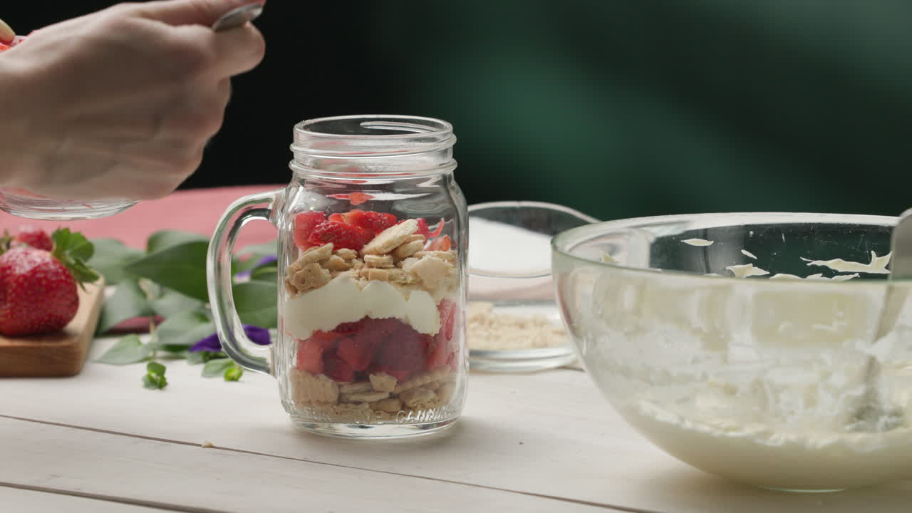 montaje del postre: agregar fresas picadas maceradas al frasco con capas de crema batida y galletas trituradas