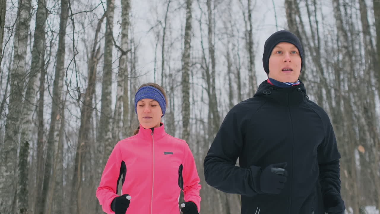 Bella e sana coppia giovane e positiva che corre in tenuta sportiva attraverso il bosco in una soleggiata mattina d'inverno