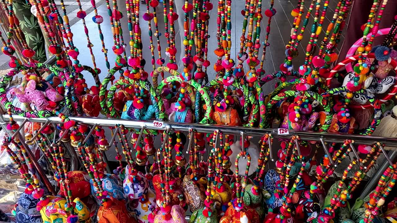 Handheld motion panning right to rows of colorful handmade traditional tourist souvenirs in a local market in Chiang mai, Thailand