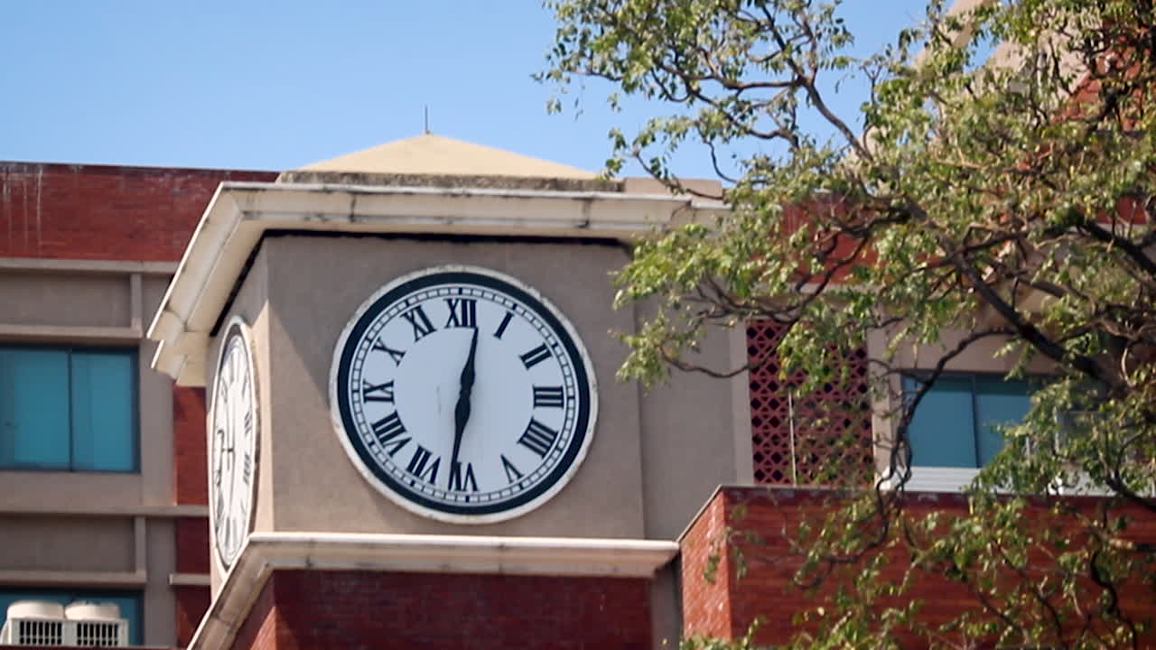 Torre del reloj en un edificio institucional en India con cielo despejado, útil para temas de educación, arquitectura, gestión del tiempo y puntos de referencia urbanos.