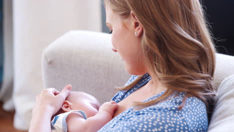 over the shoulder close up slow motion shot of mother sitting on sofa at home and breastfeeding baby