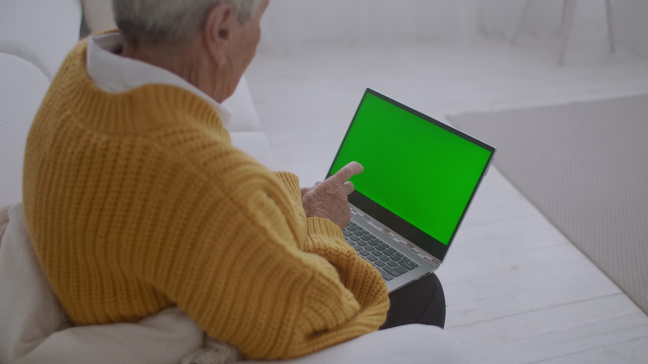 una mujer mayor mira un monitor con una pantalla verde y habla a través de un enlace de video con su nieta o hija o un médico. ayuda de video para los ancianos. la abuela usa una computadora portátil