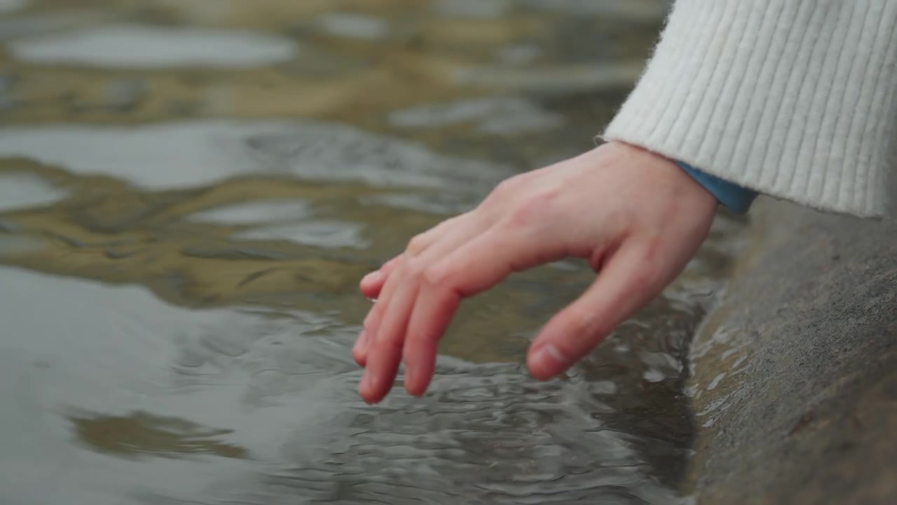 Close up of hand gently touching and creating ripples in calm water. scene focuses on interaction between human skin texture and liquid surface with soft natural lighting reflecting off