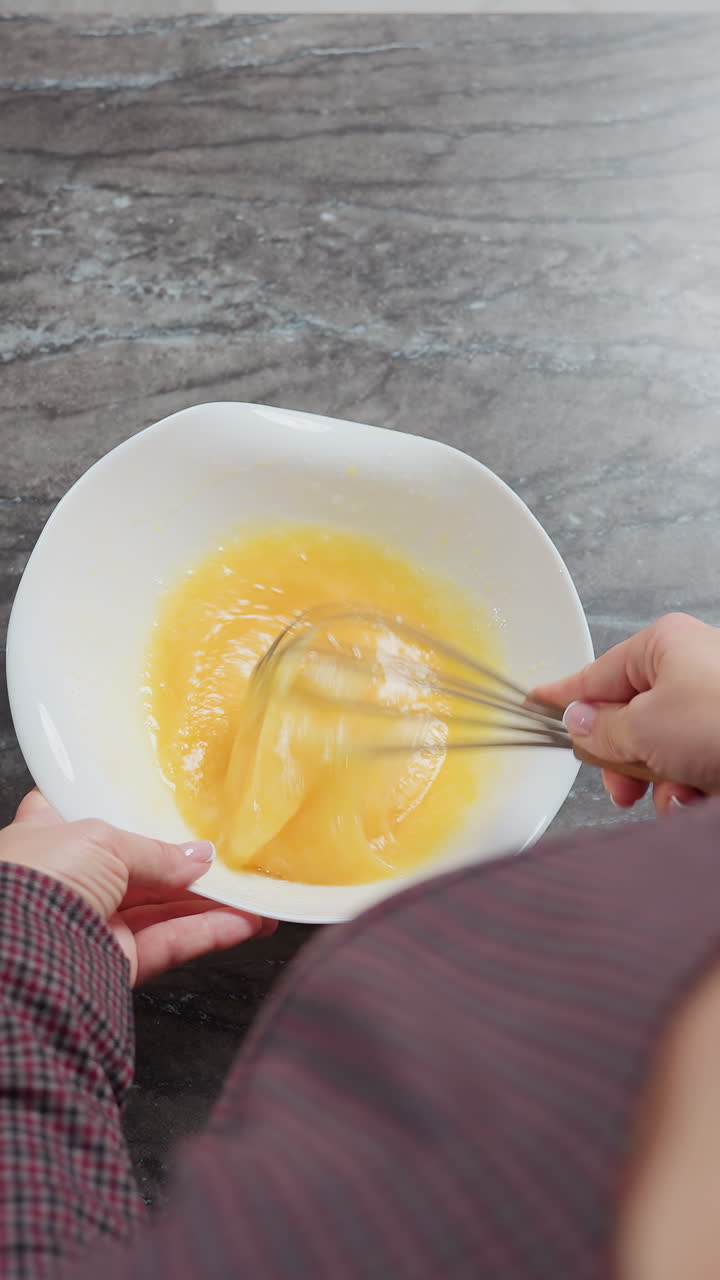vista trasera de una chica de cabello dorado que lleva un vestido a cuadros moviendo el huevo en un cuenco, ella golpea cuidadosamente la mezcla, creando una textura suave, con un mostrador de cocina limpio y luz natural suave