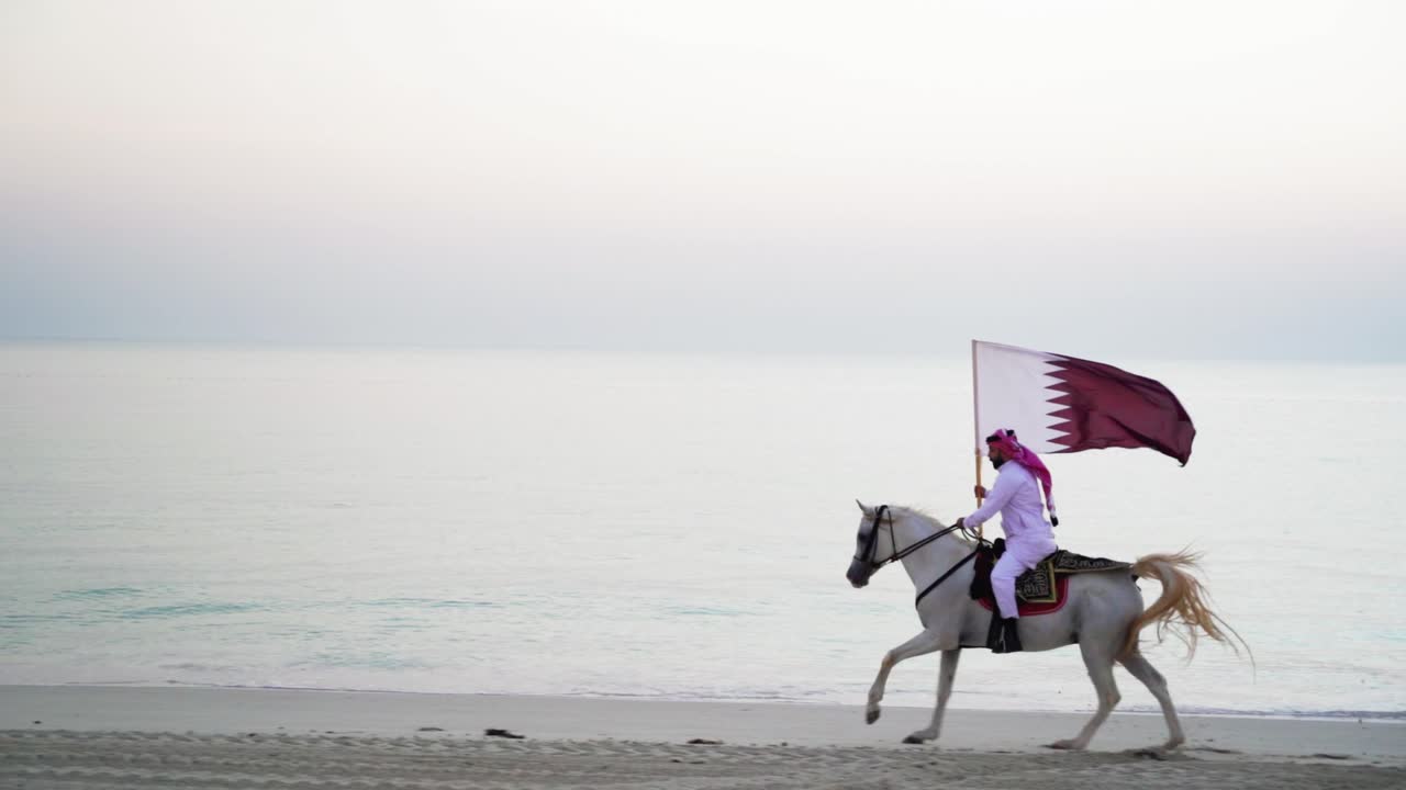 un caballero montando un caballo corriendo y sosteniendo la bandera de qatar cerca del mar