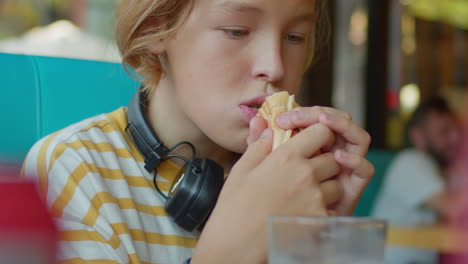 niño adolescente comiendo un perrito caliente mientras usa el teléfono