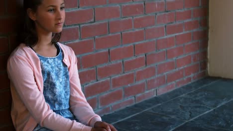 Sad-schoolgirl-sitting-against-brick-wall