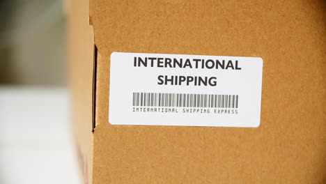 Hands-applying-INTERNATIONAL-SHIPPING-Sticker-label-on-a-cardboard-post-box-with-barcode-express