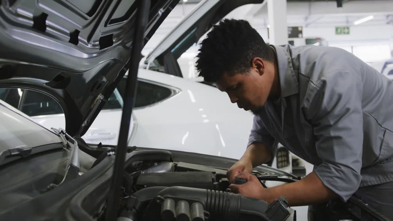mecánico de automóviles afroamericano mirando un motor de automóvil abierto y comprobando si algo está roto