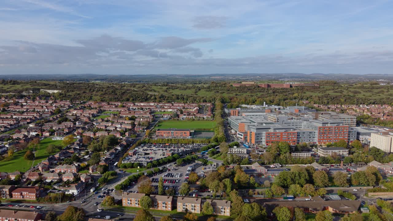 Riprese aeree frontali con drone su Portsmouth, Regno Unito, sopra case a schiera, spazi verdi e un edificio per uffici, volando verso l'interno, verso un'area urbana boscosa, in una giornata luminosa e soleggiata. Veduta urbana dettagliata
