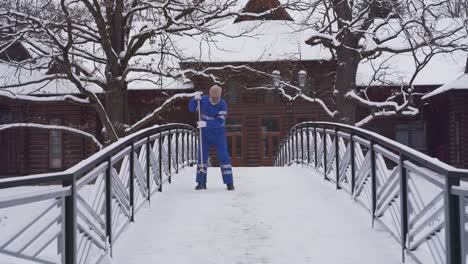 senior cleaner removing snow with broom.