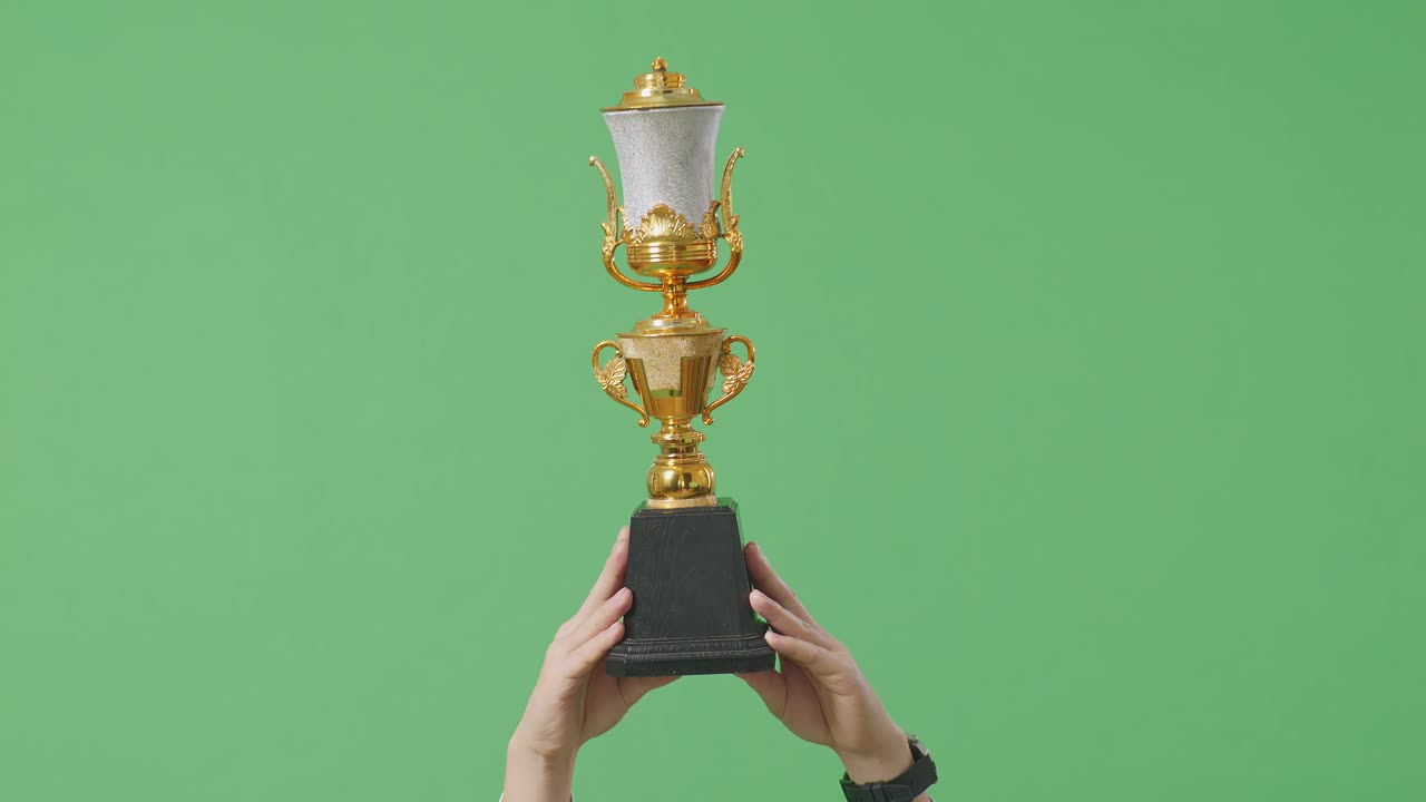 남성의 손이 공중에서 금 트로피를 들고 스튜디오의 녹색 화면 배경에서 첫 번째 우승자로 우승을 축하합니다.