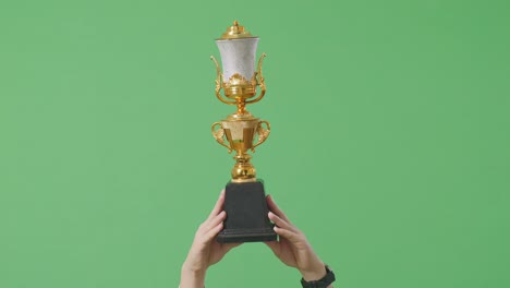 cerca de las manos del hombre sosteniendo un trofeo de oro en el aire para celebrar la victoria como el primer ganador en el fondo de la pantalla verde en el estudio