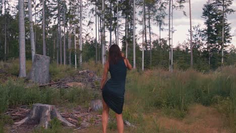 rear view of young carefree girl wearing dark blue dress dances in nature, slow motion, circle pan, sunset