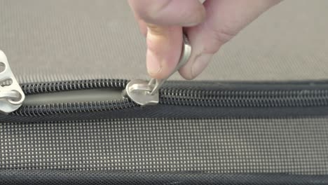 hand pulling metal zip to open suitcase close up detail