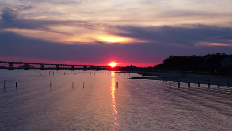 push in drone shot of beautiful pink sunset overlooking ocean and bridge in mississippi