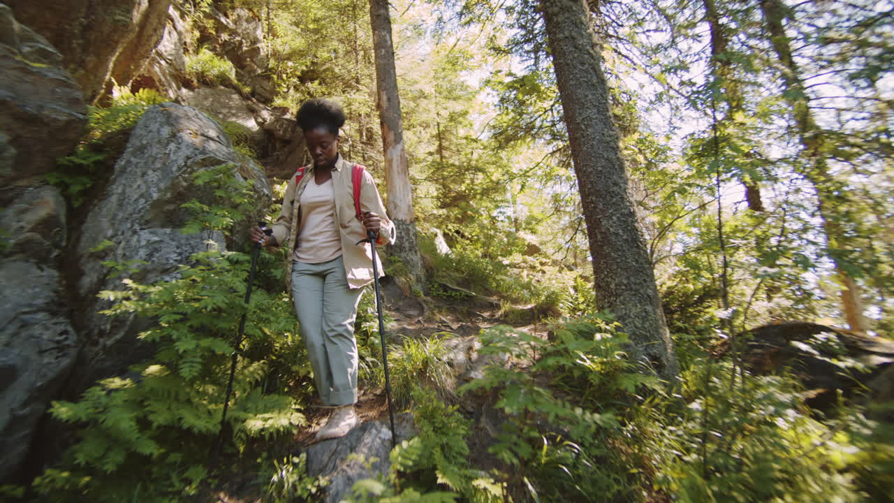 mujer negra caminando con palos de senderismo en un sendero rocoso