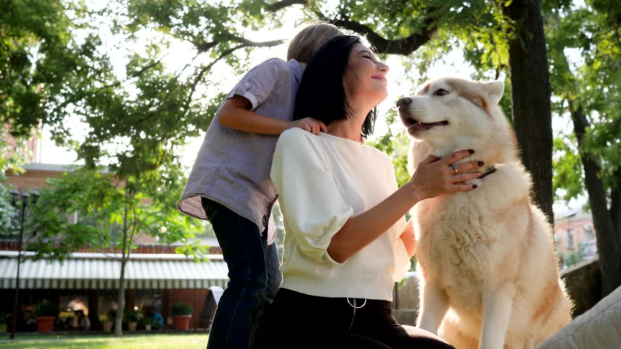 perro lamia la cara de la mujer en cámara lenta, madre con hijo y husky descansando en el parque