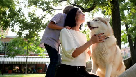 hound licks face woman in slow motion, mom with son and husky resting in park