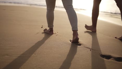Low-section-of-couple-walking-barefoot-on-the-beach.They-are-spending-time-together,-leaving-footprints-on-wet-sand