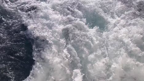 looking down at white splashing swirls on blue sea water surface from the the sailing ship