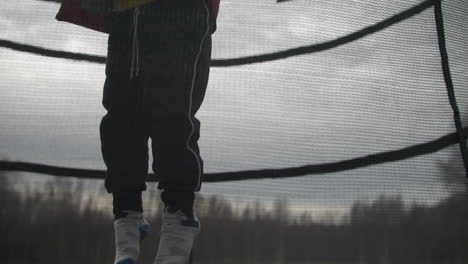 Unrecognizable-boy-jumping-on-trampoline-in-rural-area,-static-slow-motion