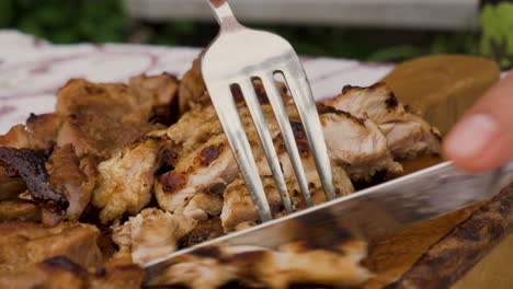 Close-shot-of-hand-holding-knife-cutting-juicy-meat-steak-on-a-wooden-board