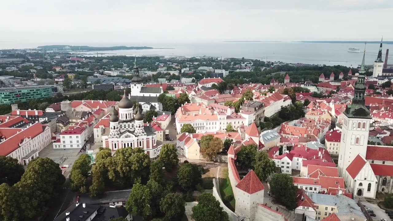 Filmato mozzafiato con drone del Centro Storico medievale di Tallinn al tramonto. L'inquadratura mostra la Collina di Toompea, la Cattedrale di Santa Maria e gli edifici dai tetti rossi sotto un cielo drammatico di nuvole rosa e arancioni.