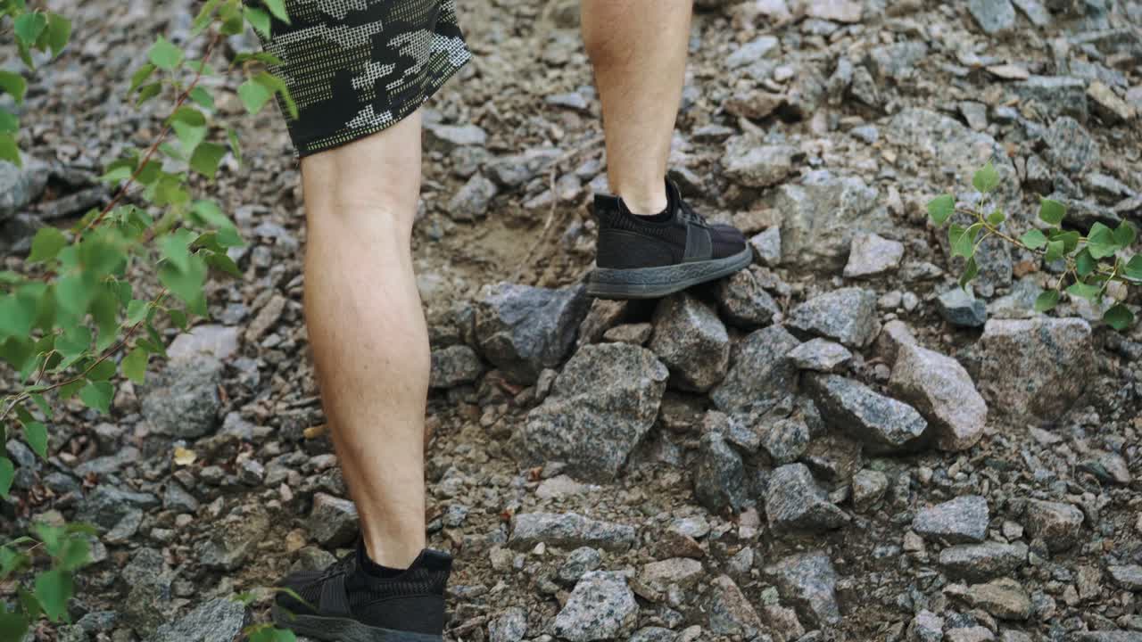 tourist with a backpack and in sneakers is climbing using his hands to the top of the cliff in the summer