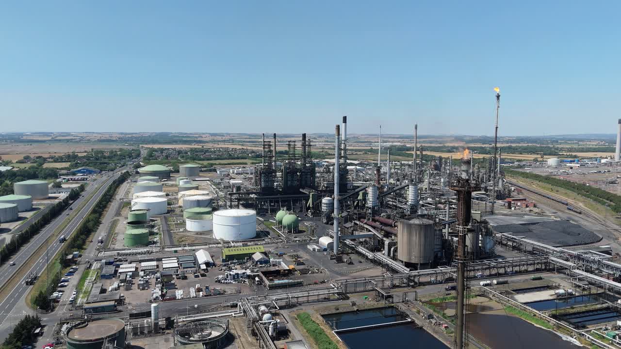 Aerial drone view of industrial chemical refinery with smoke stacks, gas flares and fuel storage silos in Immingham England UK sunny day