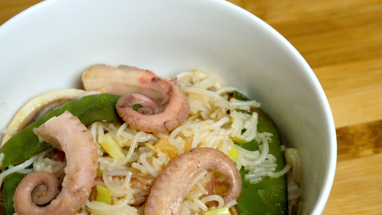 나무 표면에 있는 흰색 문어 그릇과 국수의 회전 샷