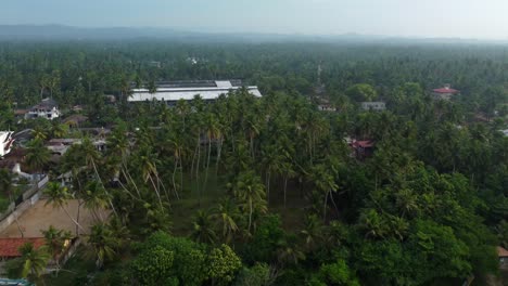 Retirada-Aérea-De-La-Ciudad-Rural-Rodeada-De-Un-Frondoso-Bosque-Con-Neblina-Matutina-En-La-Distancia,-Sri-Lanka