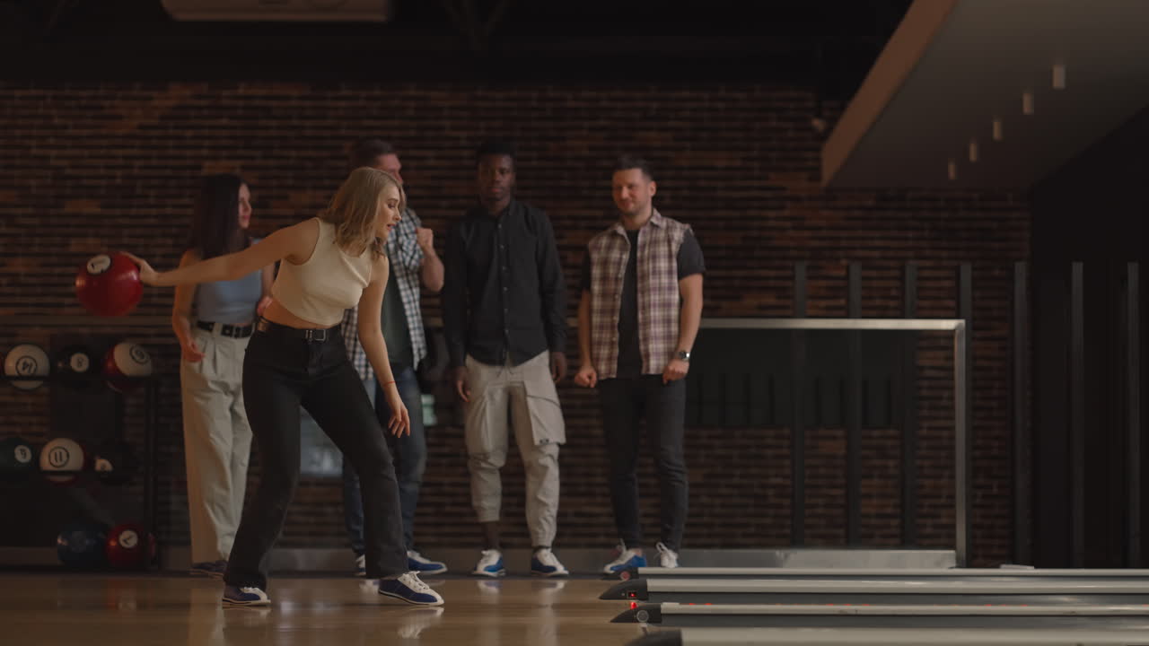 Giocatrice di bowling lancia la palla con il supporto degli amici e festeggia dopo aver fatto strike.