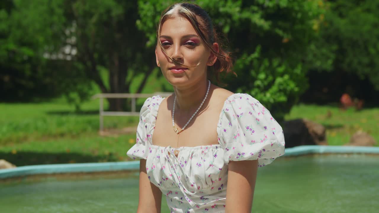 A girl in a light, flowing dress wanders through a tropical park on a sunny day.
