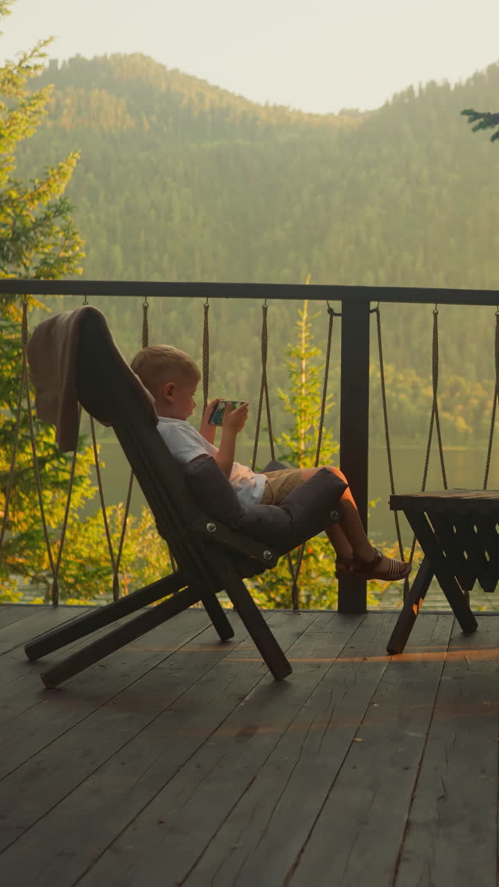hermana y hermano se sientan en la terraza soleada jugando videojuegos. niño y niña disfrutan de una agradable mañana de fin de semana contra una impresionante vista de las montañas