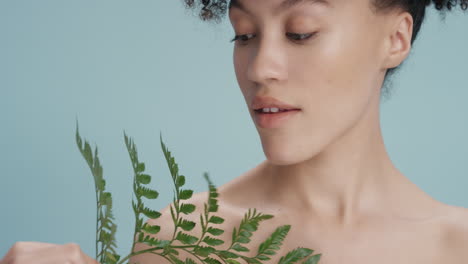 close up portrait beautiful mixed race woman touching skin with leaf caressing smooth healthy complexion enjoying playful natural beauty on blue background skincare concept