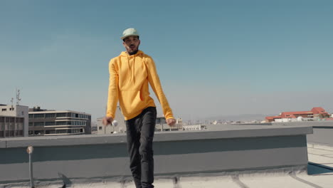 dancing man hip hop dancer performing freestyle dance moves on rooftop in city wearing yellow hoodie